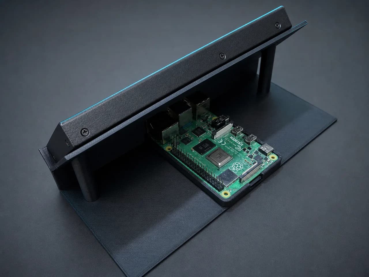 The prototype seen from behind with its enclosure open, showing the single-board computer mounted on the 3D-printed base that holds the display panel at a reading angle.